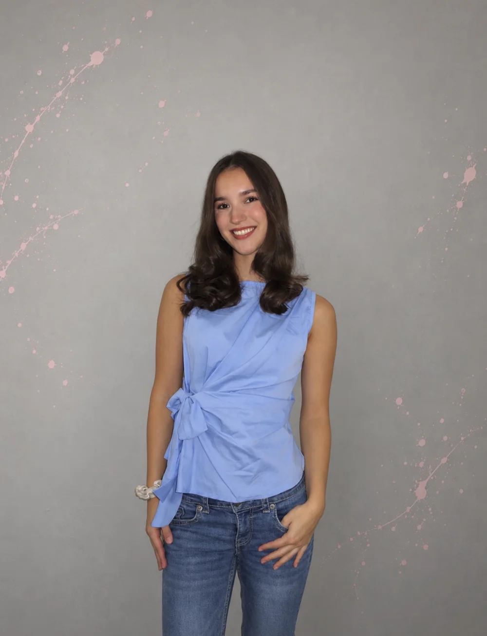 Amalia lächelt vor einer grauen Wand mit rosa Farbspritzern